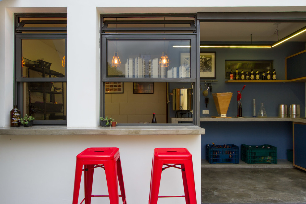 Photo of a mid-sized industrial l-shaped seated home bar in Other with a drop-in sink, flat-panel cabinets, blue cabinets, concrete benchtops, blue splashback, concrete floors, grey floor and grey benchtop.