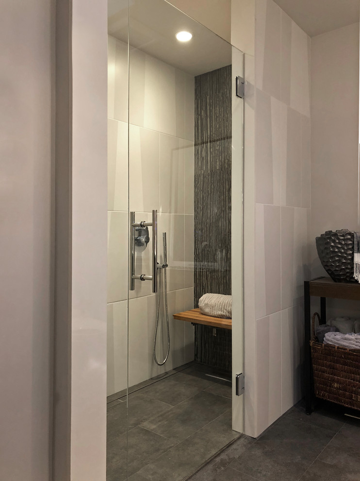 This is an example of a mid-sized modern 3/4 bathroom in Seattle with glass-front cabinets, grey cabinets, a curbless shower, a wall-mount toilet, black and white tile, stone tile, white walls, porcelain floors, an integrated sink, glass benchtops, grey floor, a hinged shower door and grey benchtops.