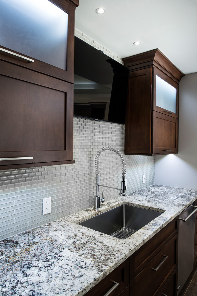 Example of a large transitional ceramic tile and beige floor eat-in kitchen design with an undermount sink, shaker cabinets, brown cabinets, granite countertops, stainless steel appliances, an island, white backsplash and glass tile backsplash