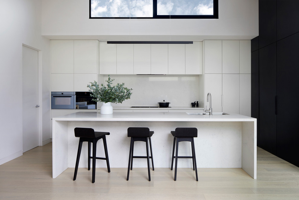 Cette photo montre une cuisine ouverte moderne avec un évier encastré, des portes de placard blanches, un plan de travail en quartz modifié, une crédence en quartz modifié et îlot.
