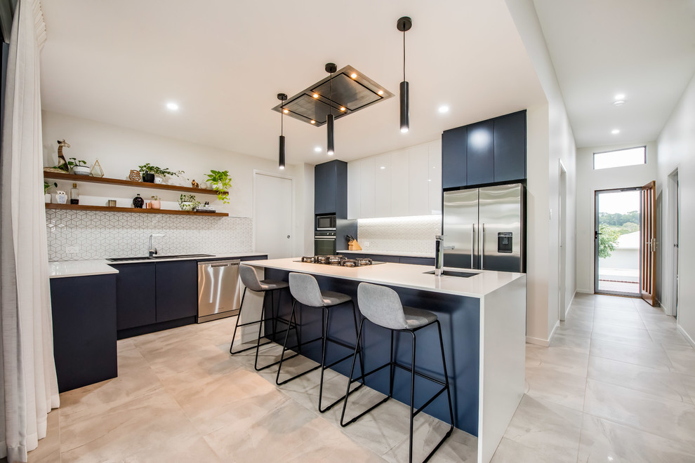 Mid-sized contemporary u-shaped open plan kitchen in Other with a drop-in sink, flat-panel cabinets, blue cabinets, white splashback, stainless steel appliances, with island, grey floor, white benchtop, granite benchtops, ceramic splashback and ceramic floors.