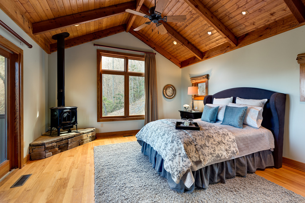 This is an example of a large country master bedroom in Chicago with beige walls, light hardwood floors, a wood stove and brown floor.