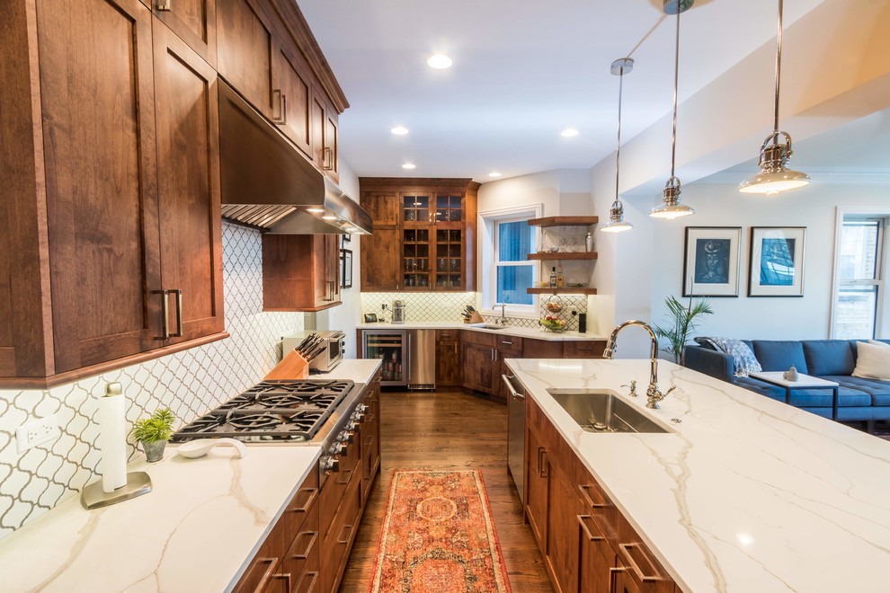 Large traditional l-shaped open plan kitchen in Chicago with medium hardwood floors, an undermount sink, white benchtop, shaker cabinets, dark wood cabinets, quartz benchtops, white splashback, porcelain splashback, stainless steel appliances, with island and brown floor.