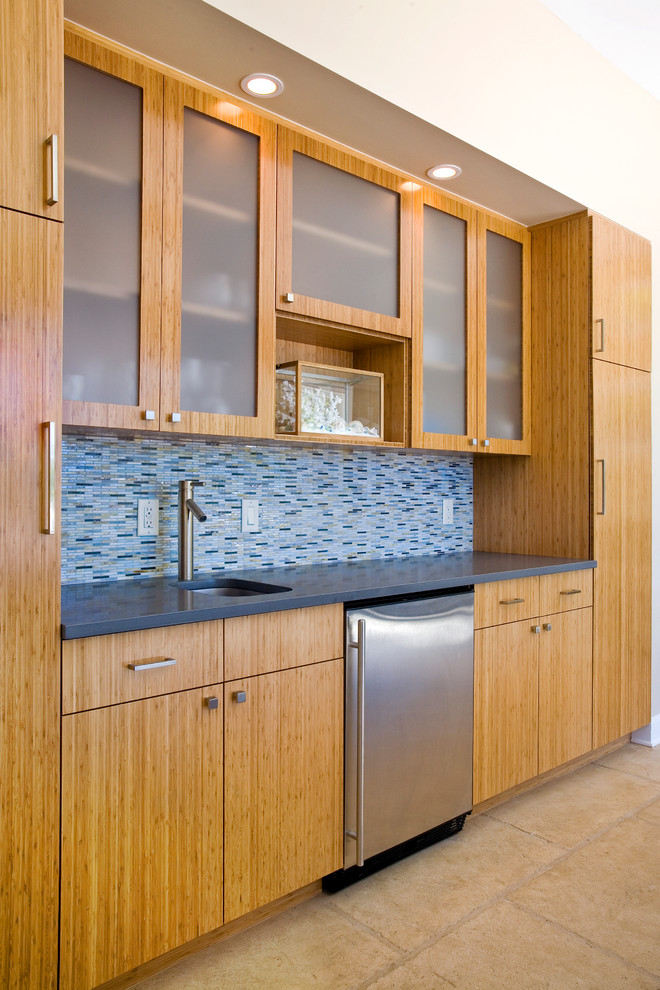 Design ideas for a mid-sized transitional single-wall wet bar in Austin with an undermount sink, flat-panel cabinets, light wood cabinets, solid surface benchtops, blue splashback, matchstick tile splashback, porcelain floors and blue benchtop.