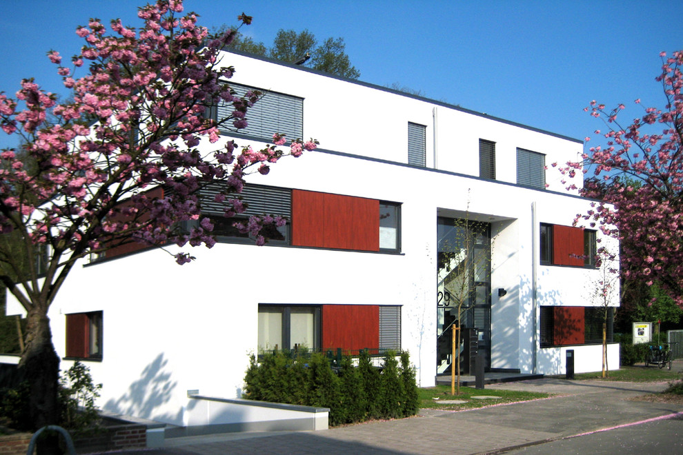 Design ideas for a mid-sized contemporary three-storey stucco white apartment exterior in Dortmund with a flat roof.