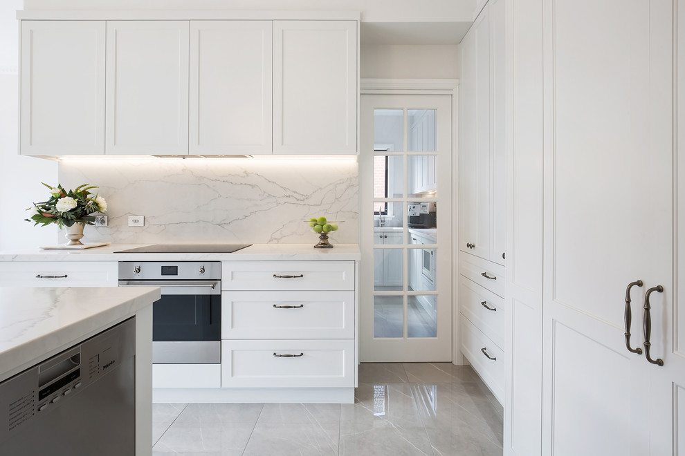 Photo of a large traditional l-shaped open plan kitchen in Sydney with an undermount sink, shaker cabinets, beige cabinets, quartz benchtops, grey splashback, stone slab splashback, stainless steel appliances, porcelain floors, with island, brown floor and white benchtop.