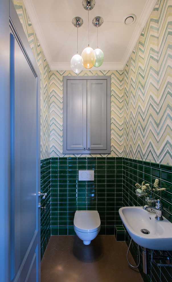 This is an example of a mid-sized transitional powder room in Moscow with a wall-mount toilet, green tile, ceramic tile, green walls, ceramic floors, brown floor and a wall-mount sink.