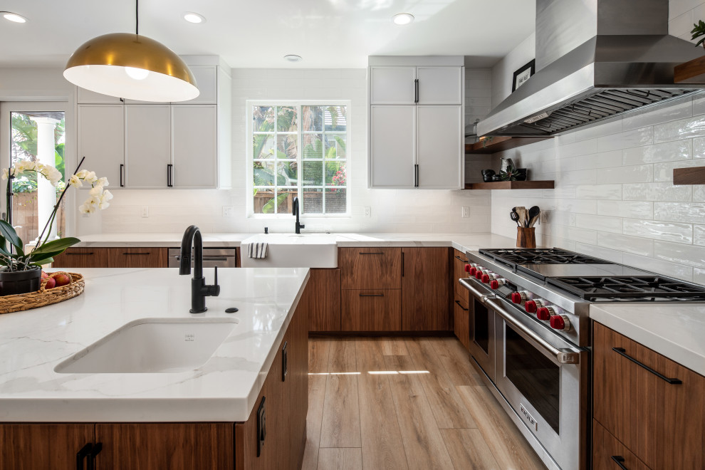 This is an example of a medium sized midcentury u-shaped open plan kitchen in San Diego with a belfast sink, flat-panel cabinets, medium wood cabinets, marble worktops, white splashback, ceramic splashback, stainless steel appliances, laminate floors, an island, beige floors and white worktops.