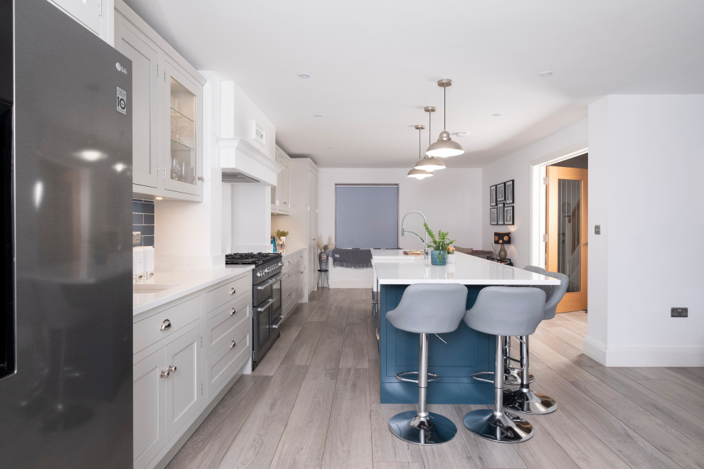 Photo of a large classic single-wall open plan kitchen in Other with a built-in sink, shaker cabinets, quartz worktops, blue splashback, ceramic splashback, laminate floors, an island, white worktops and a chimney breast.