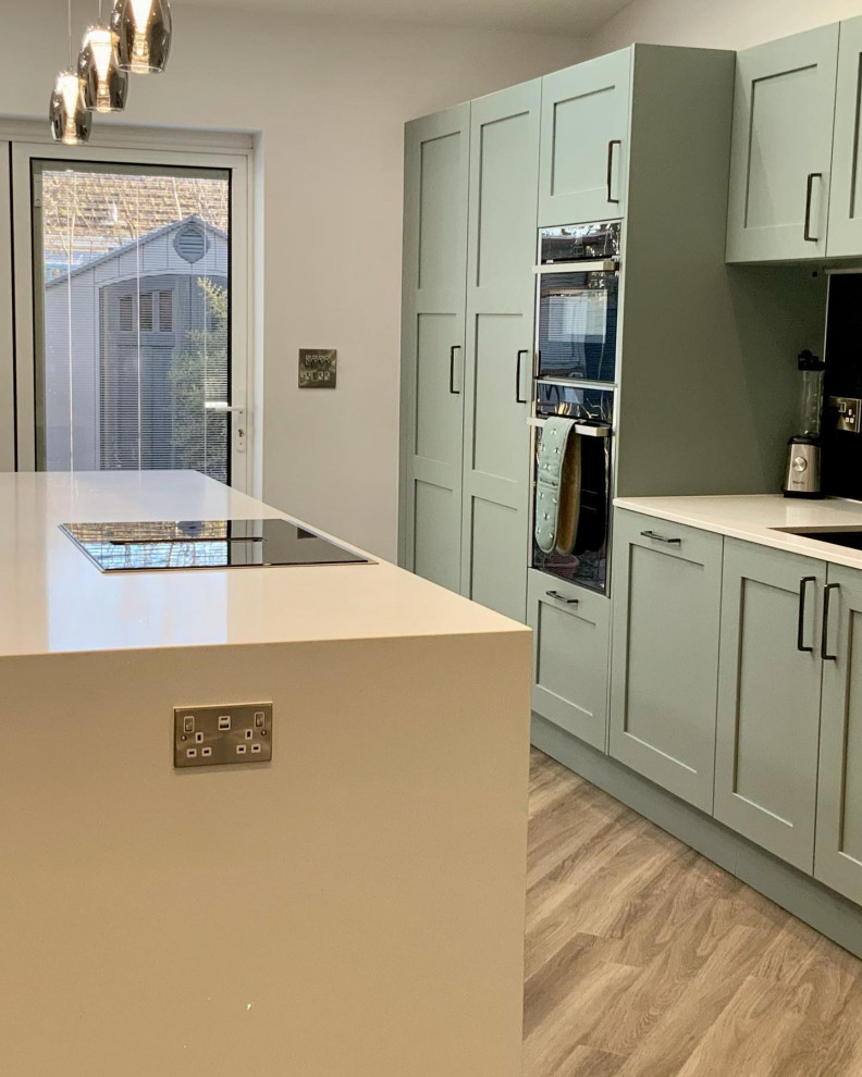 Inspiration for a large traditional galley open plan kitchen with shaker cabinets, green cabinets, quartzite benchtops, mirror splashback, panelled appliances, vinyl floors, with island, brown floor and white benchtop.