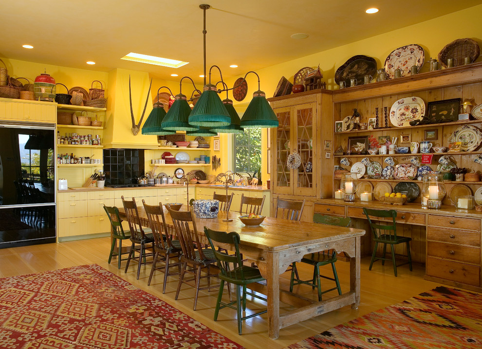 This is an example of an eclectic l-shaped eat-in kitchen in Santa Barbara with flat-panel cabinets, yellow cabinets, black splashback and black appliances.