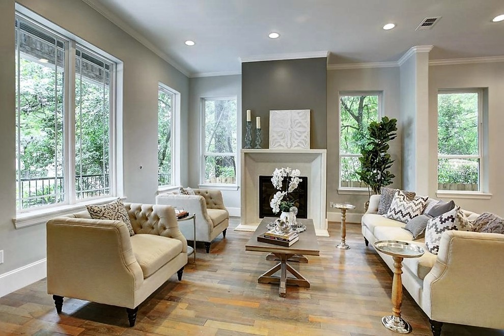 Photo of a mid-sized transitional formal open concept living room in Houston with grey walls, light hardwood floors, a standard fireplace, a concrete fireplace surround and no tv.