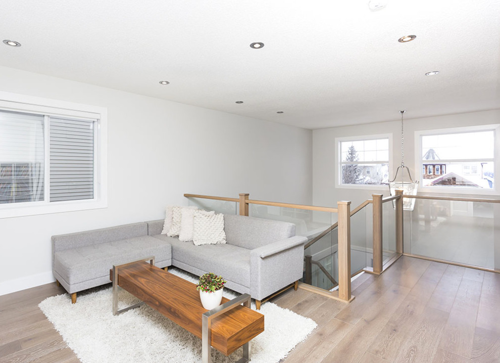 This is an example of a mid-sized scandinavian open concept family room in Calgary with white walls, light hardwood floors, no fireplace and brown floor.