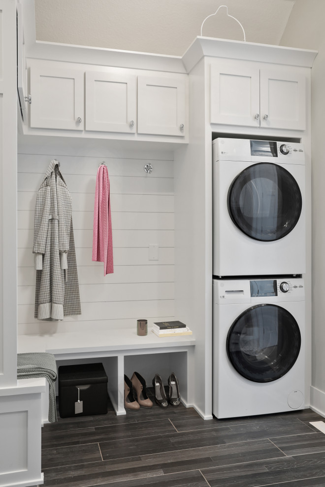Small single-wall utility room in Minneapolis with shaker cabinets, white cabinets, white walls, dark hardwood floors, a stacked washer and dryer, grey floor and wood walls.