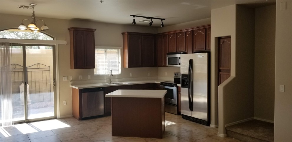 Small transitional l-shaped porcelain tile and brown floor open concept kitchen photo in Phoenix with an undermount sink, raised-panel cabinets, dark wood cabinets, laminate countertops, stainless steel appliances, an island and white countertops