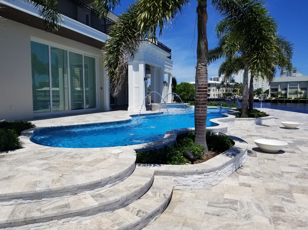 This is an example of a large modern backyard custom-shaped pool in Miami with a hot tub and natural stone pavers.