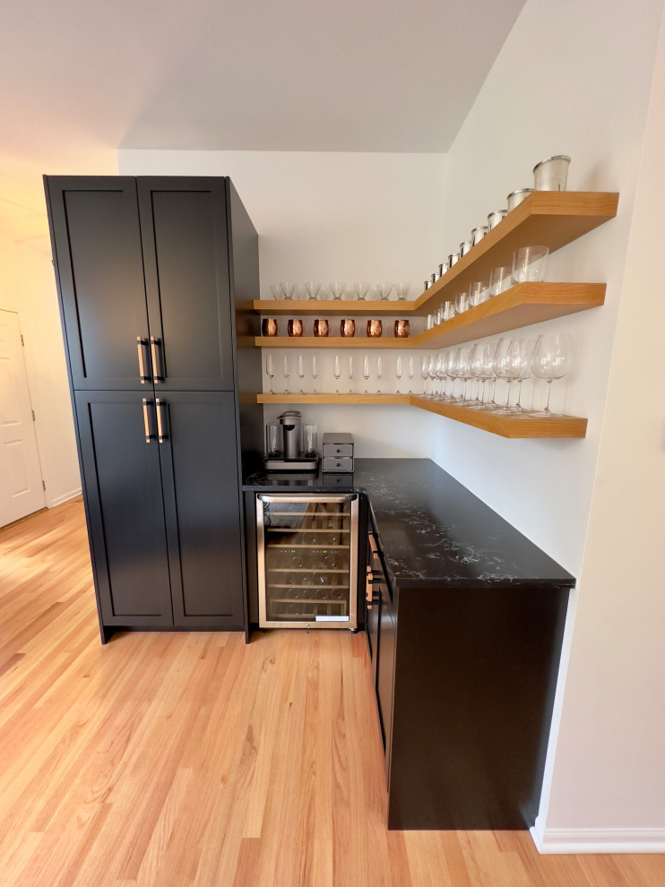 Inspiration for a small contemporary l-shaped dry bar in Chicago with shaker cabinets, black cabinets, engineered stone countertops, light hardwood flooring, orange floors and black worktops.
