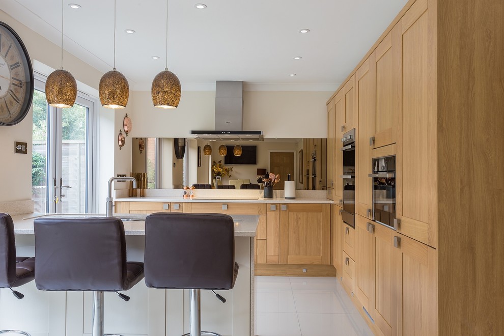Inspiration for a mid-sized transitional u-shaped eat-in kitchen in Hertfordshire with shaker cabinets, light wood cabinets, quartzite benchtops, metallic splashback, glass sheet splashback and a peninsula.
