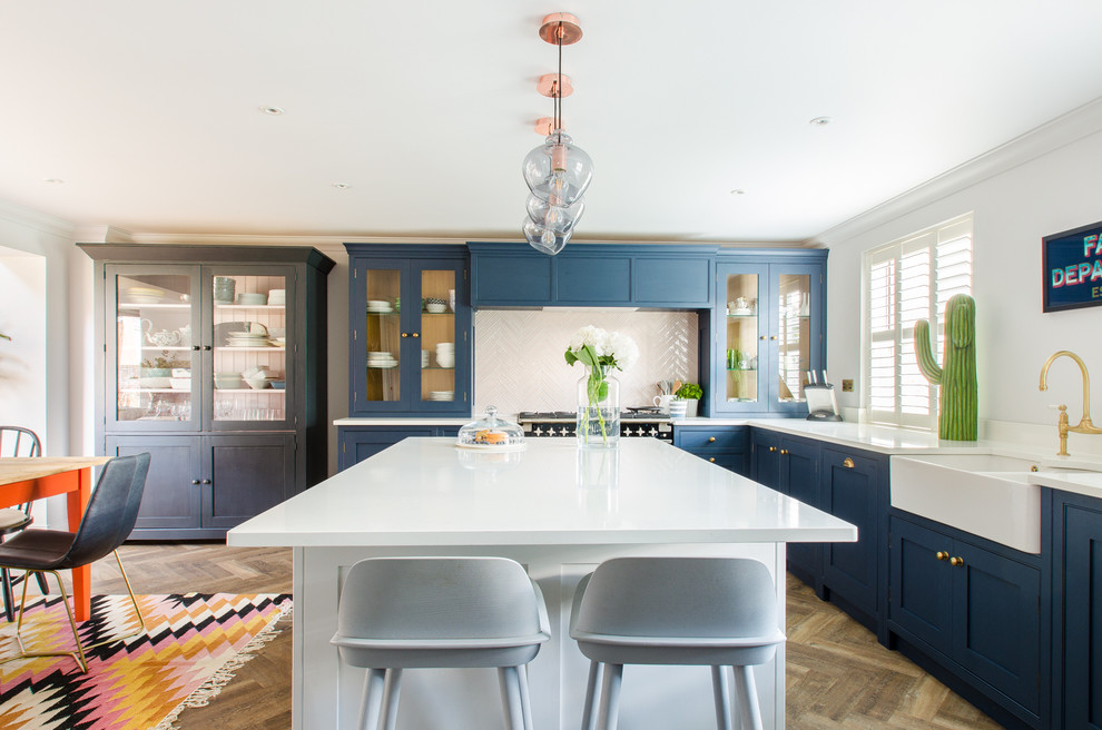 Mid-sized transitional l-shaped eat-in kitchen in Kent with beaded inset cabinets, solid surface benchtops, white splashback, medium hardwood floors, with island, brown floor, a double-bowl sink and blue cabinets.