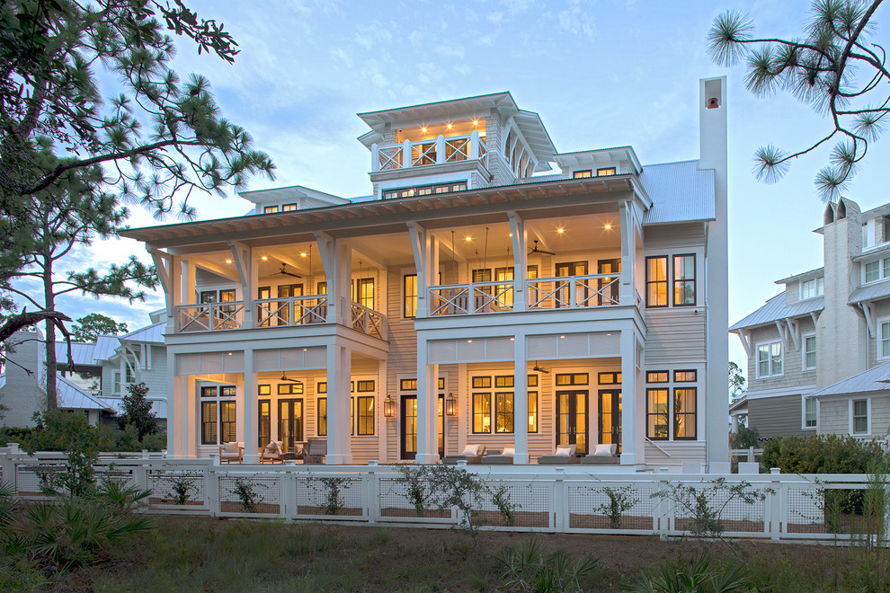Photo of a beach style three-storey beige house exterior in Miami with a gable roof and a metal roof.