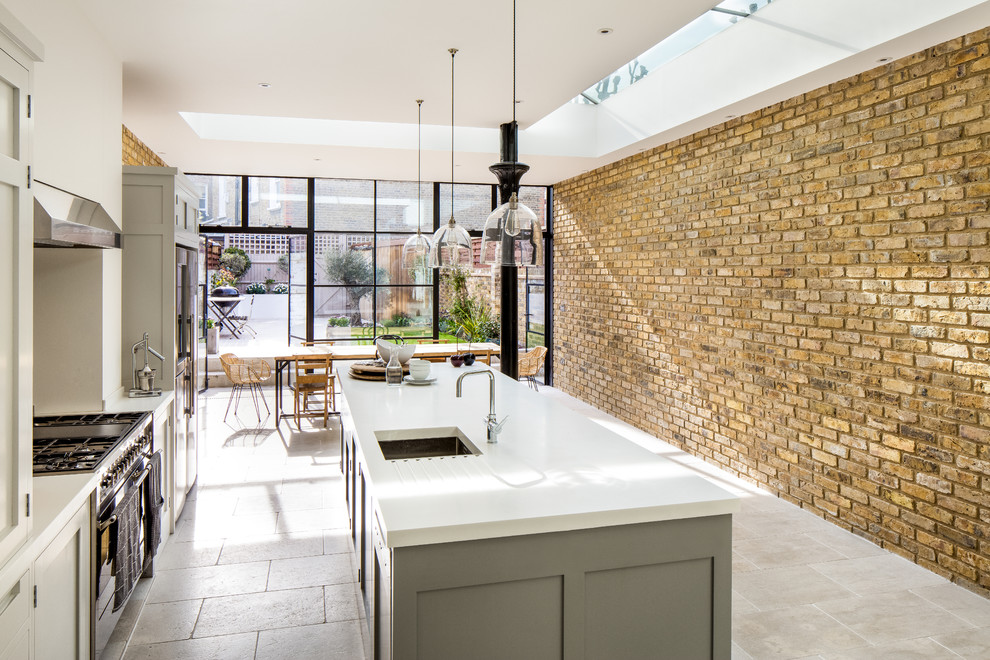 Photo of a mid-sized transitional eat-in kitchen in London with an integrated sink, shaker cabinets, grey cabinets, solid surface benchtops, stainless steel appliances, limestone floors and with island.