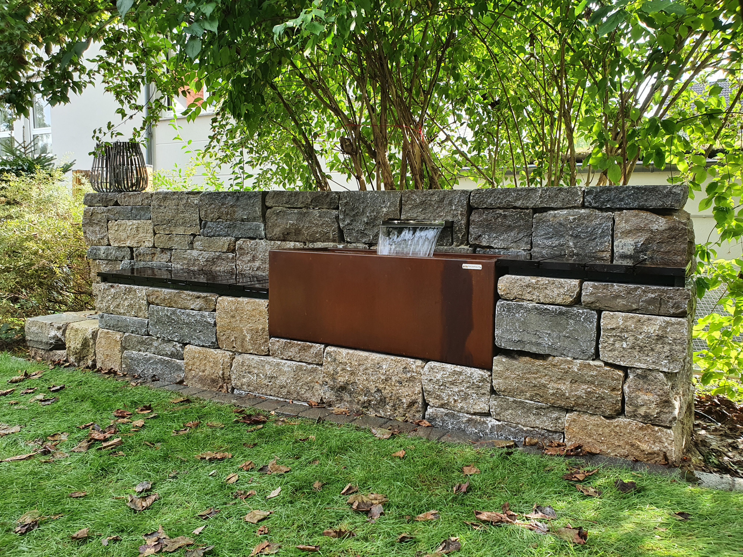 Natursteinmauer mit Wasserspiel und Sitzgelegenheiten