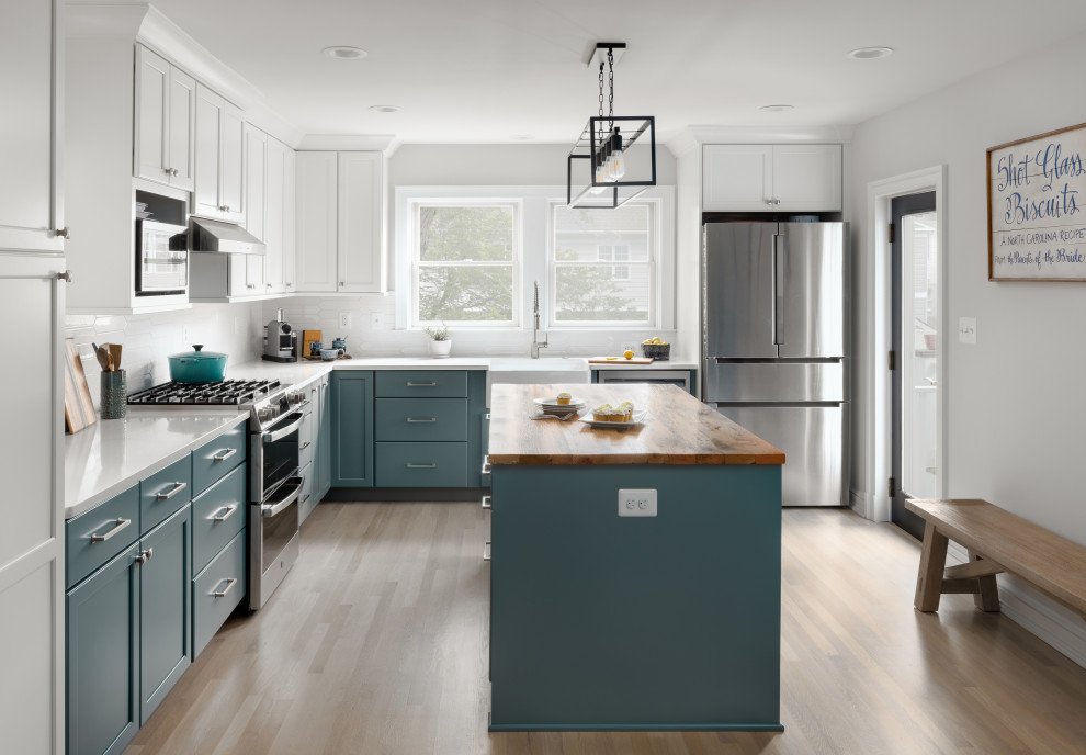 Mid-sized transitional l-shaped kitchen in DC Metro with a farmhouse sink, shaker cabinets, green cabinets, quartz benchtops, white splashback, ceramic splashback, stainless steel appliances, light hardwood floors, with island, white benchtop and exposed beam.