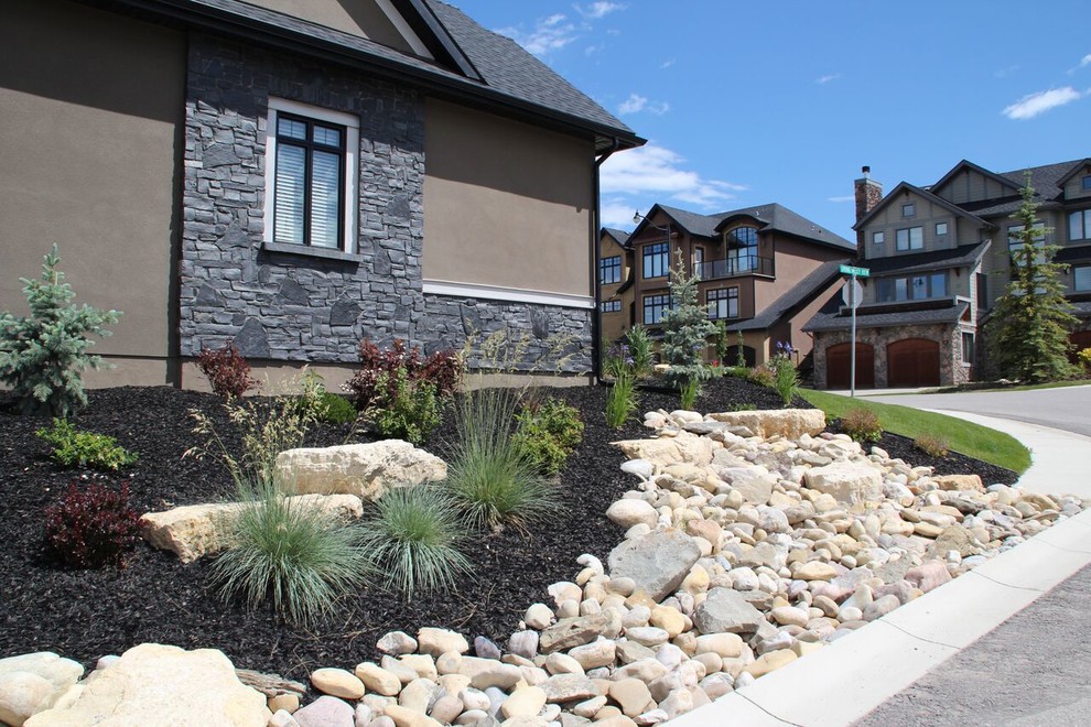Photo of a mid-sized transitional front yard full sun garden in Calgary with a retaining wall and natural stone pavers.