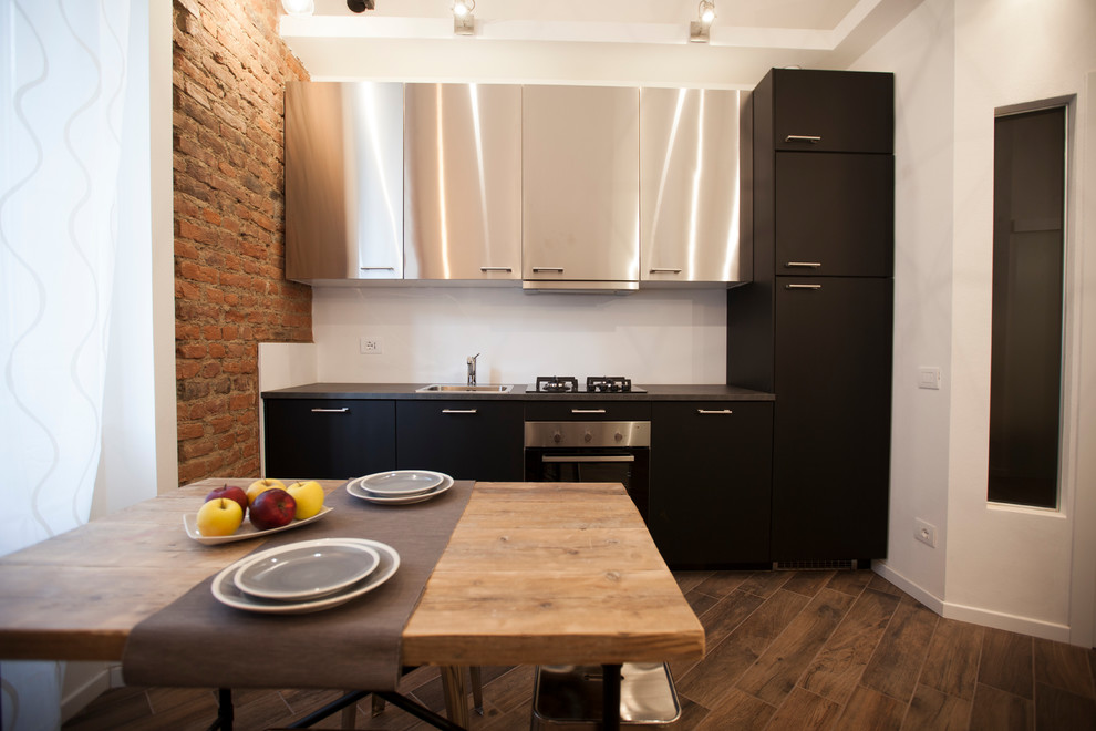Mid-sized industrial single-wall open plan kitchen in Milan with a drop-in sink, stainless steel cabinets, stainless steel appliances, porcelain floors, no island, brown floor and flat-panel cabinets.