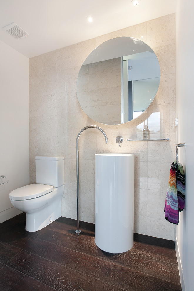 This is an example of a mid-sized modern powder room in Melbourne with a pedestal sink, black tile, stone tile, medium hardwood floors, beige walls and a two-piece toilet.