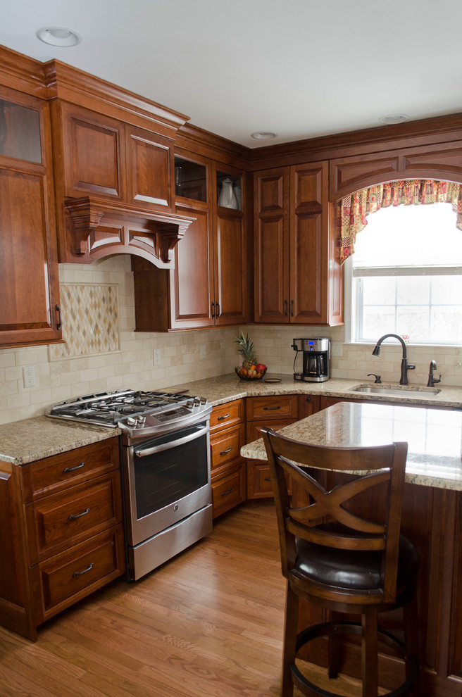 This is an example of a mid-sized traditional l-shaped eat-in kitchen in Philadelphia with a single-bowl sink, raised-panel cabinets, medium wood cabinets, granite benchtops, beige splashback, stone tile splashback, stainless steel appliances, medium hardwood floors and with island.