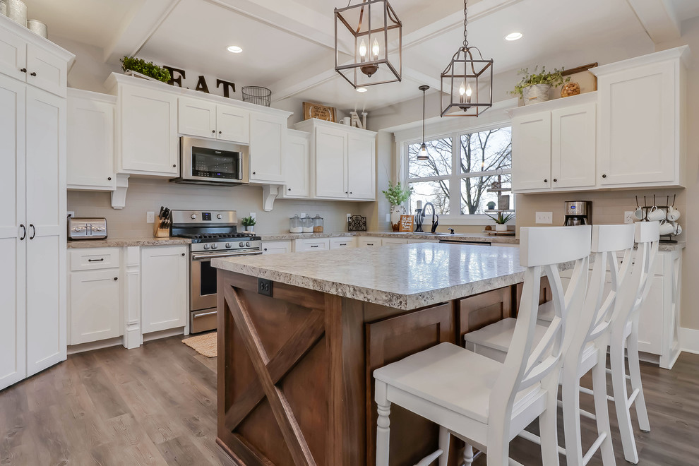 This is an example of a large country u-shaped open plan kitchen in Grand Rapids with a drop-in sink, shaker cabinets, white cabinets, beige splashback, porcelain splashback, stainless steel appliances, medium hardwood floors, with island, brown floor and beige benchtop.