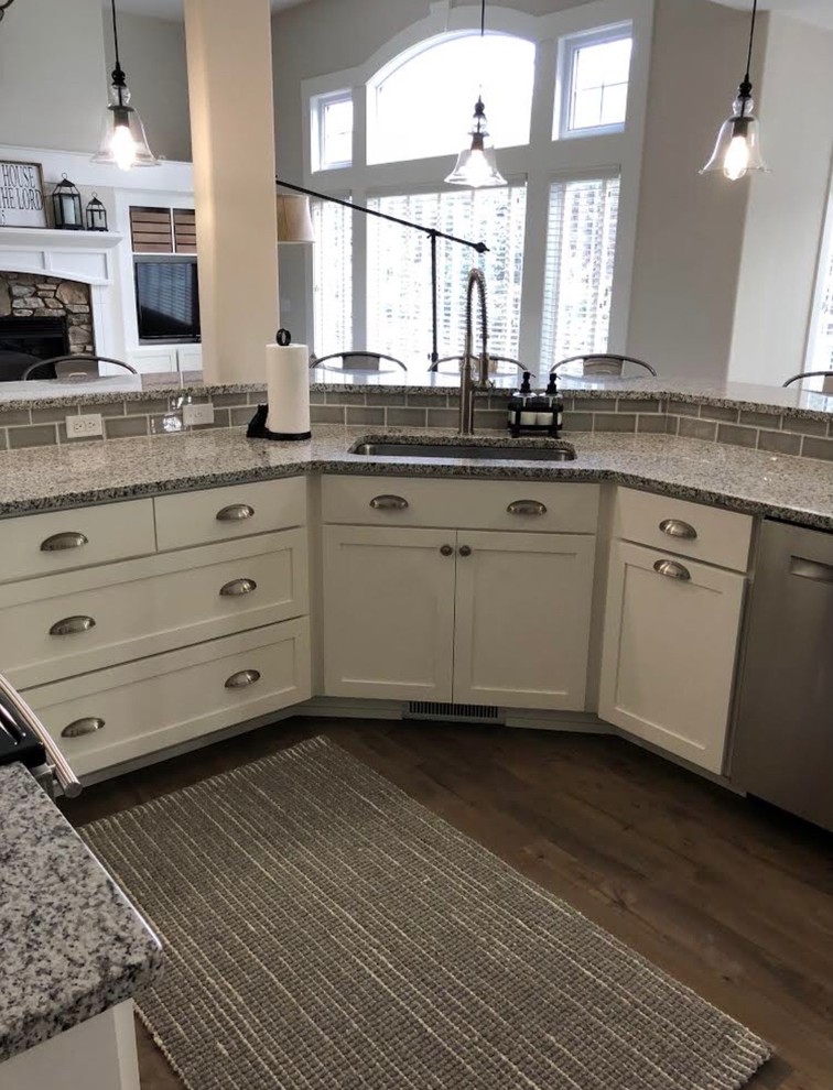 Inspiration for a mid-sized contemporary open plan kitchen in Grand Rapids with shaker cabinets, white cabinets, granite benchtops, grey splashback, subway tile splashback, stainless steel appliances, dark hardwood floors, a peninsula, brown floor and an undermount sink.
