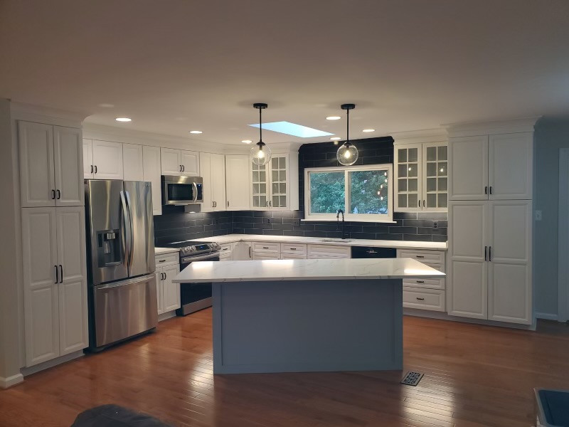 This is an example of a large modern l-shaped eat-in kitchen in DC Metro with a drop-in sink, shaker cabinets, white cabinets, quartzite benchtops, black splashback, subway tile splashback, stainless steel appliances, light hardwood floors, multiple islands, brown floor and white benchtop.