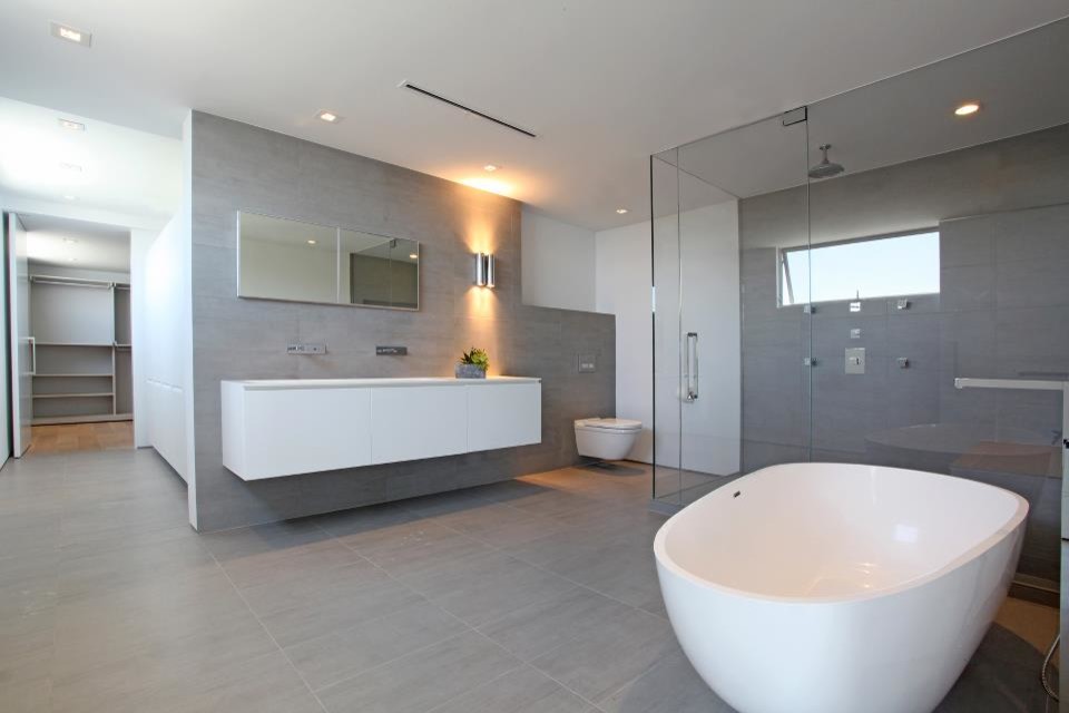 Design ideas for a large modern master bathroom in Los Angeles with flat-panel cabinets, white cabinets, a freestanding tub, a corner shower, a wall-mount toilet, gray tile, grey walls, a wall-mount sink, grey floor, a hinged shower door, white benchtops, a double vanity, a floating vanity and recessed.