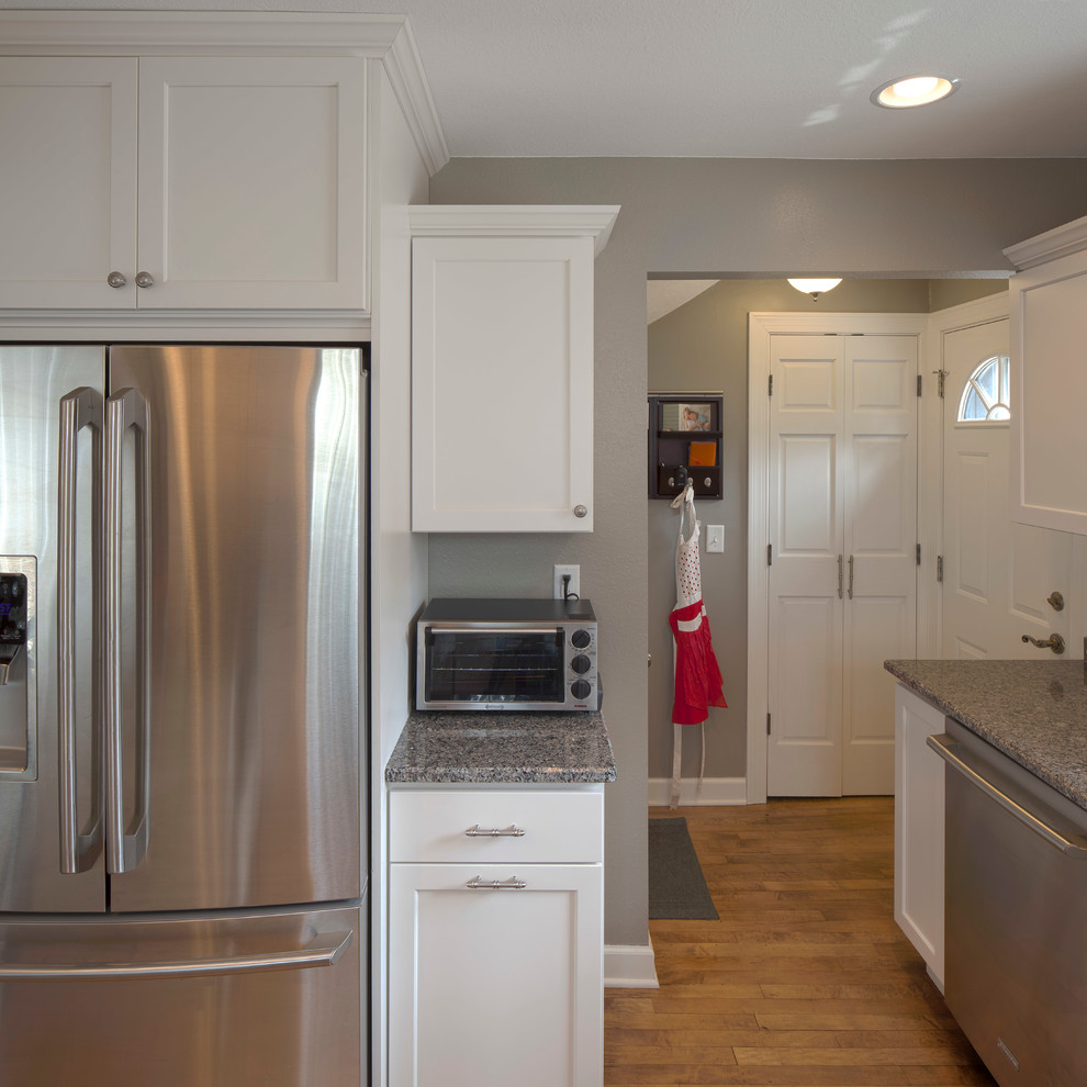 Photo of a traditional separate kitchen in Milwaukee with an undermount sink, raised-panel cabinets, white cabinets, granite benchtops, stainless steel appliances, light hardwood floors and a peninsula.