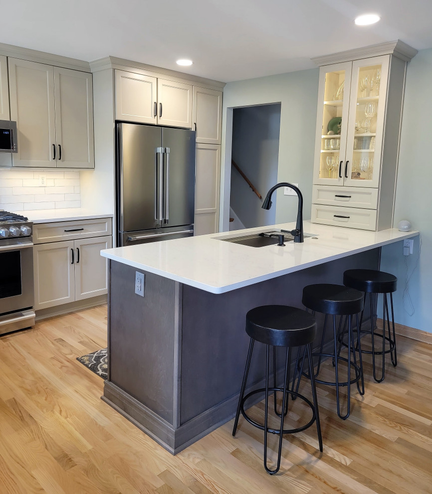Eat-in kitchen - mid-sized transitional l-shaped medium tone wood floor and yellow floor eat-in kitchen idea with an undermount sink, flat-panel cabinets, gray cabinets, quartz countertops, white backsplash, ceramic backsplash, stainless steel appliances, an island and white countertops