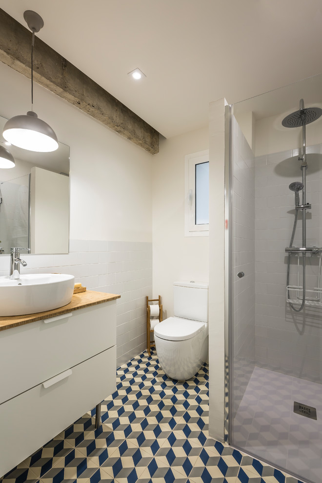 Small contemporary 3/4 bathroom in Valencia with flat-panel cabinets, white cabinets, white tile, ceramic tile, white walls, ceramic floors, an integrated sink, multi-coloured floor, a corner shower, a one-piece toilet, wood benchtops, a hinged shower door and brown benchtops.