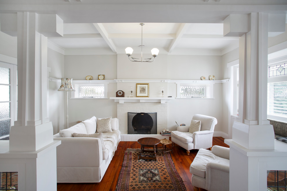 Traditional formal open concept living room in Auckland with medium hardwood floors, a brick fireplace surround, no tv, grey walls and a standard fireplace.