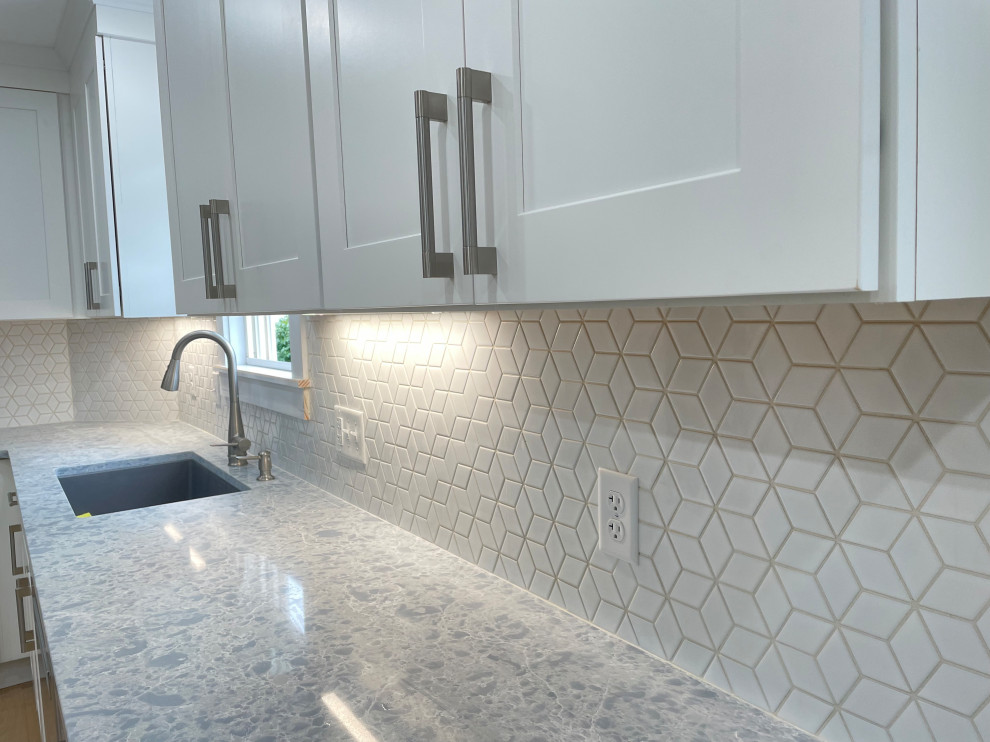 Inspiration for a large transitional l-shaped light wood floor and brown floor kitchen pantry remodel in Boston with an undermount sink, shaker cabinets, white cabinets, quartz countertops, white backsplash, ceramic backsplash, stainless steel appliances, no island and gray countertops