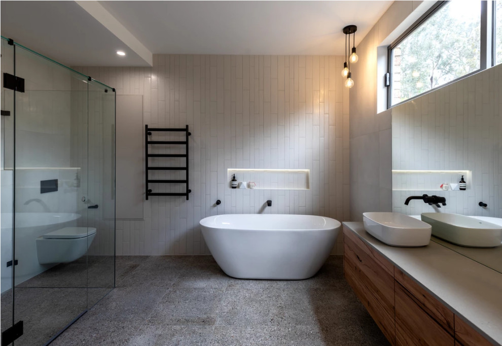 Inspiration for a large modern bathroom in Melbourne with flat-panel cabinets, medium wood cabinets, a freestanding tub, a one-piece toilet, white tile, ceramic tile, white walls, terrazzo floors, a vessel sink, engineered quartz benchtops, grey floor, a hinged shower door, a niche, a double vanity, a floating vanity, vaulted and grey benchtops.