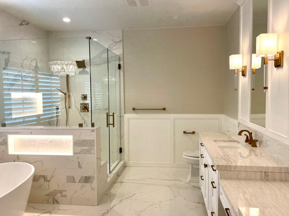 Inspiration for a large traditional master bathroom in Orange County with recessed-panel cabinets, white cabinets, a freestanding tub, a corner shower, a two-piece toilet, multi-coloured tile, porcelain tile, beige walls, porcelain floors, an undermount sink, solid surface benchtops, multi-coloured floor, a hinged shower door, beige benchtops, a shower seat, a double vanity, a built-in vanity and decorative wall panelling.
