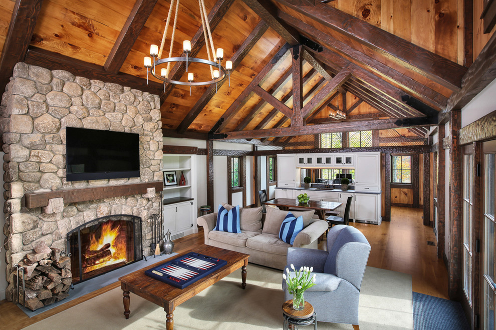 Country open concept living room in New York with grey walls, medium hardwood floors, a standard fireplace, a stone fireplace surround and a wall-mounted tv.