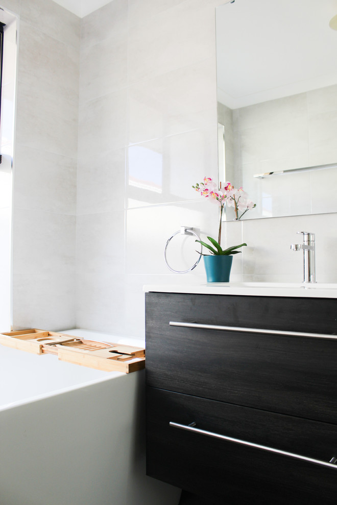 This is an example of a small kids bathroom in Perth with flat-panel cabinets, dark wood cabinets, a freestanding tub, a corner shower, gray tile, porcelain tile, grey walls, porcelain floors, an integrated sink, solid surface benchtops, grey floor, a hinged shower door and white benchtops.