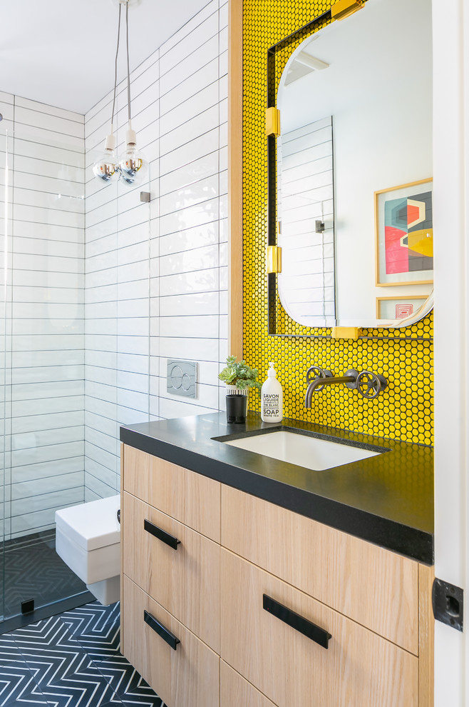 This is an example of a mid-sized contemporary bathroom in Orange County with flat-panel cabinets, light wood cabinets, a wall-mount toilet, yellow tile, mosaic tile, white walls, an undermount sink, black floor and black benchtops.