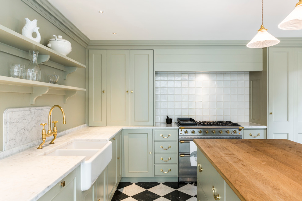 Traditional l-shaped open plan kitchen in London with a farmhouse sink, beaded inset cabinets, green cabinets, marble benchtops, white splashback, ceramic splashback, stainless steel appliances, marble floors and with island.