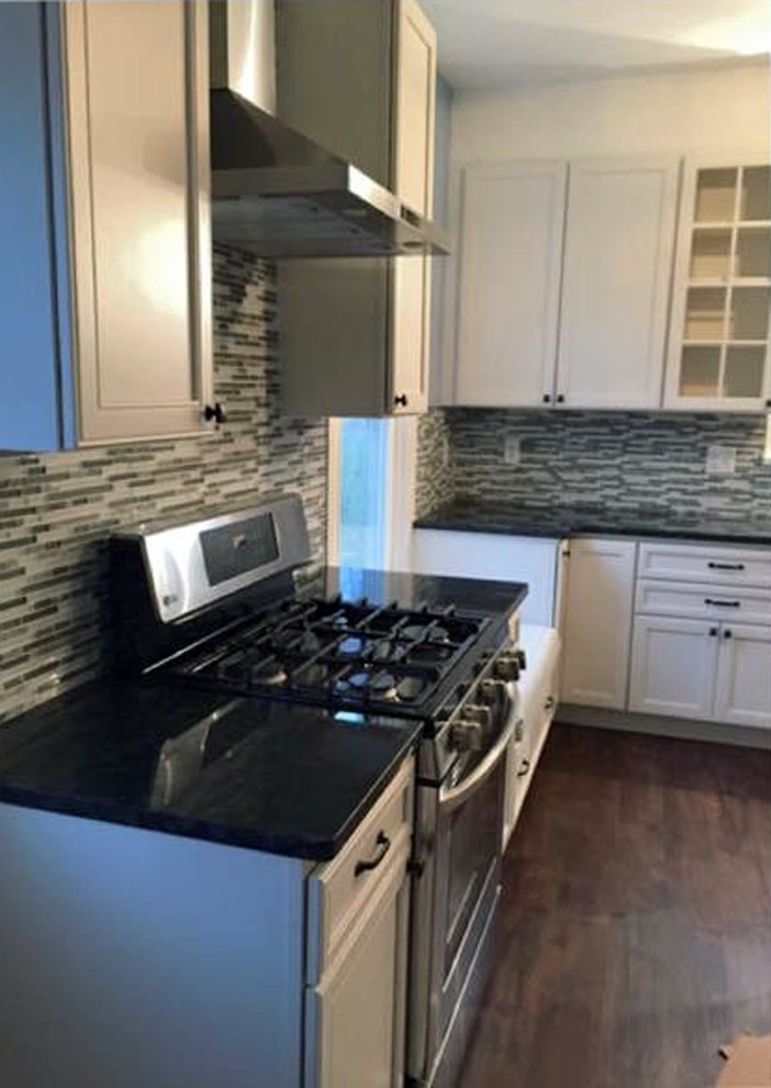 Kitchen pantry - mid-sized transitional l-shaped medium tone wood floor and brown floor kitchen pantry idea with a farmhouse sink, recessed-panel cabinets, white cabinets, granite countertops, multicolored backsplash, glass tile backsplash, stainless steel appliances, no island and black countertops