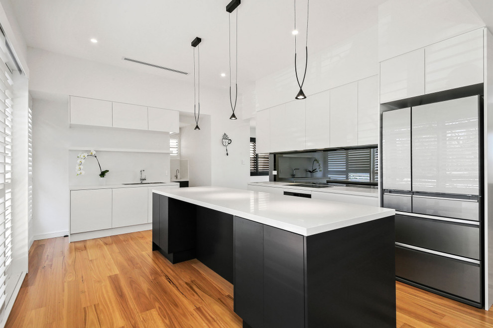Design ideas for an expansive contemporary l-shaped eat-in kitchen in Sydney with flat-panel cabinets, white cabinets, quartz benchtops, glass sheet splashback, stainless steel appliances, medium hardwood floors, with island, brown floor and white benchtop.