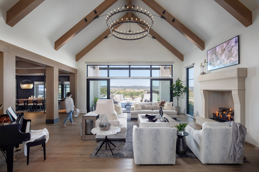 Great Room Living Room Family Room Design with Fireplace and Built-in Bookshelf - The great room of this luxury custom home features an oversized stone fireplace, built-in bookshelf and firewood niche, luxury furnishings including cream swivel chairs, gray sofas and an oversized light wood coffee table. High ceilings and a mix of materials make this a showstopping living room.