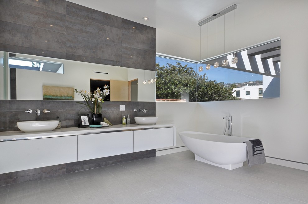 This is an example of a large contemporary bathroom in Los Angeles with a vessel sink, flat-panel cabinets, white cabinets, a freestanding tub, gray tile and white walls.